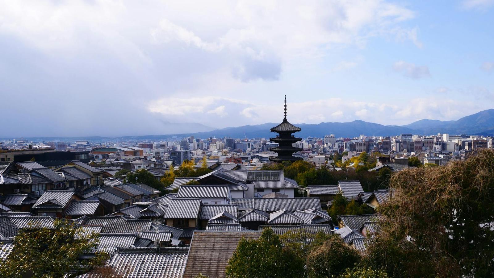 Wooden pagoda rising above tiled rooftops with a city skyline behind
