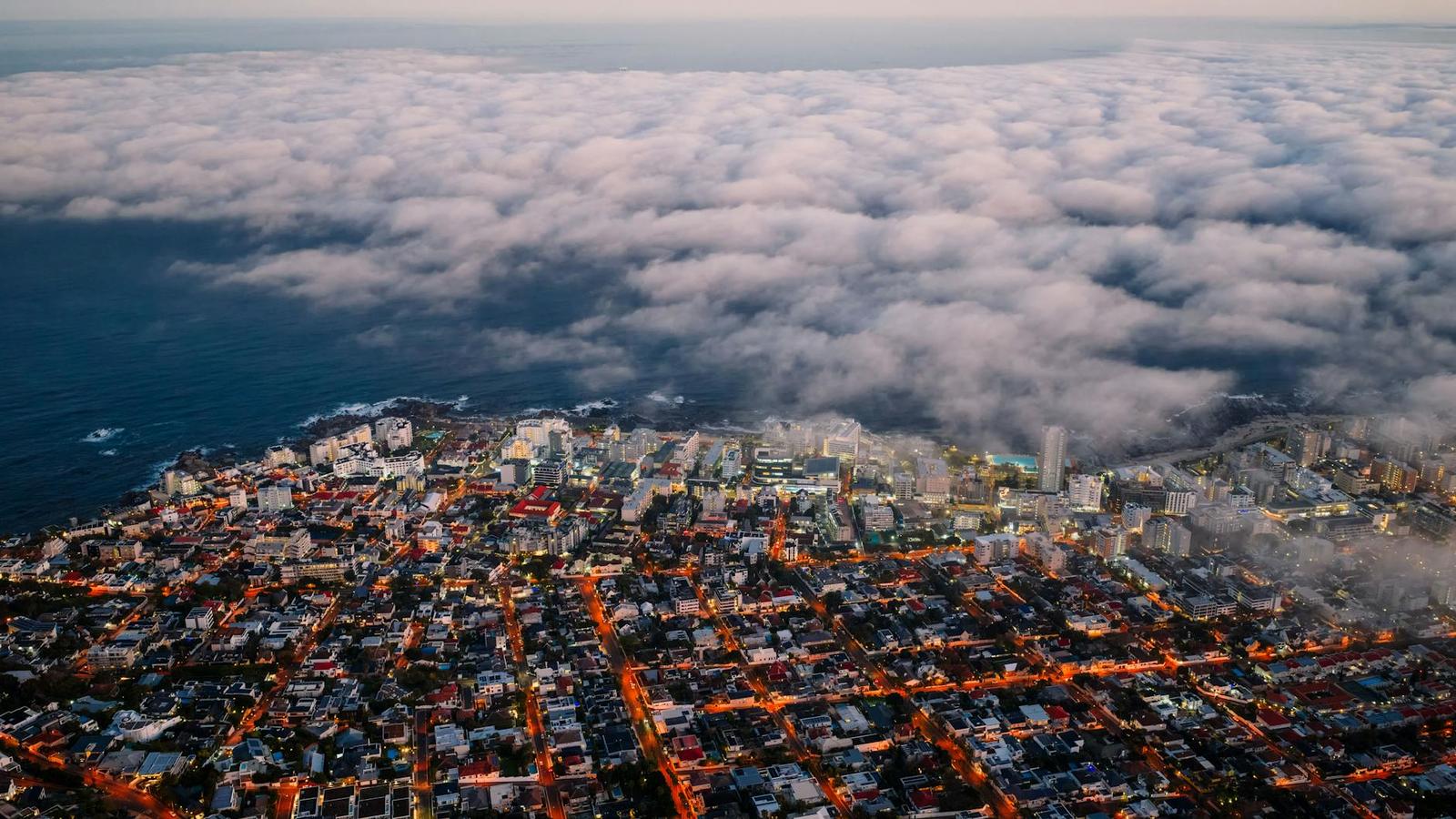A blanket of sea fog rolls over a coastal city at dusk