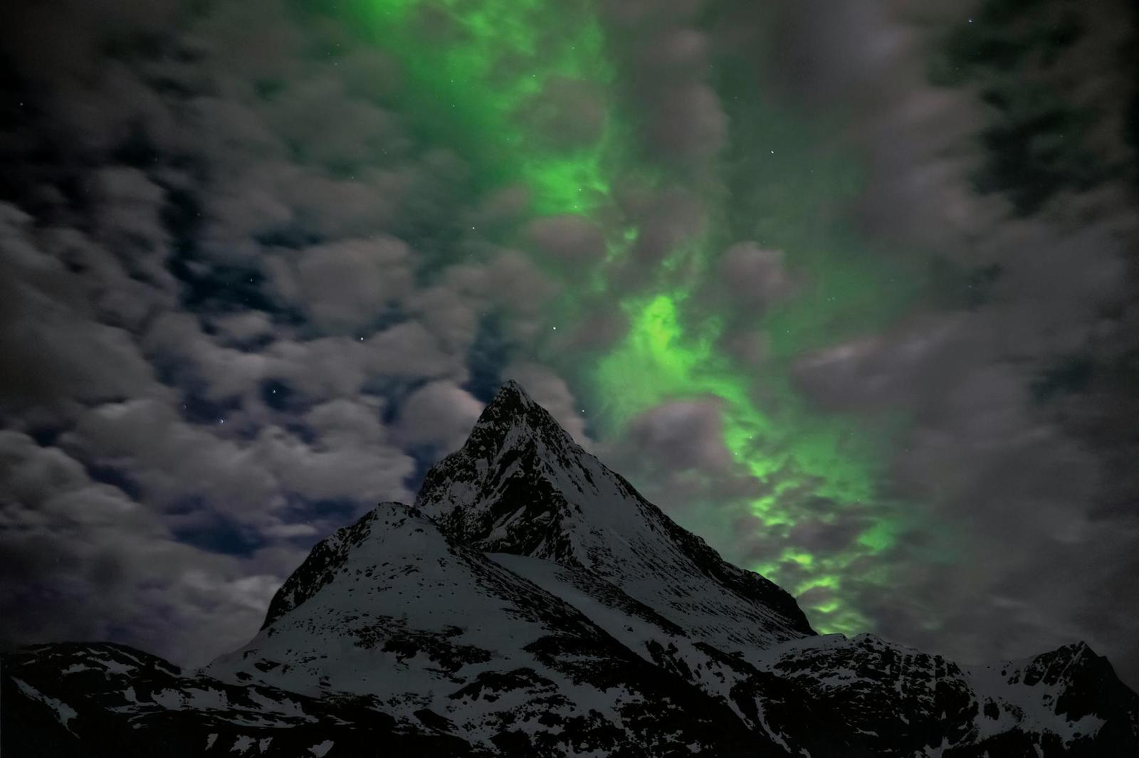 Green aurora swirling above a snow-capped mountain peak at night