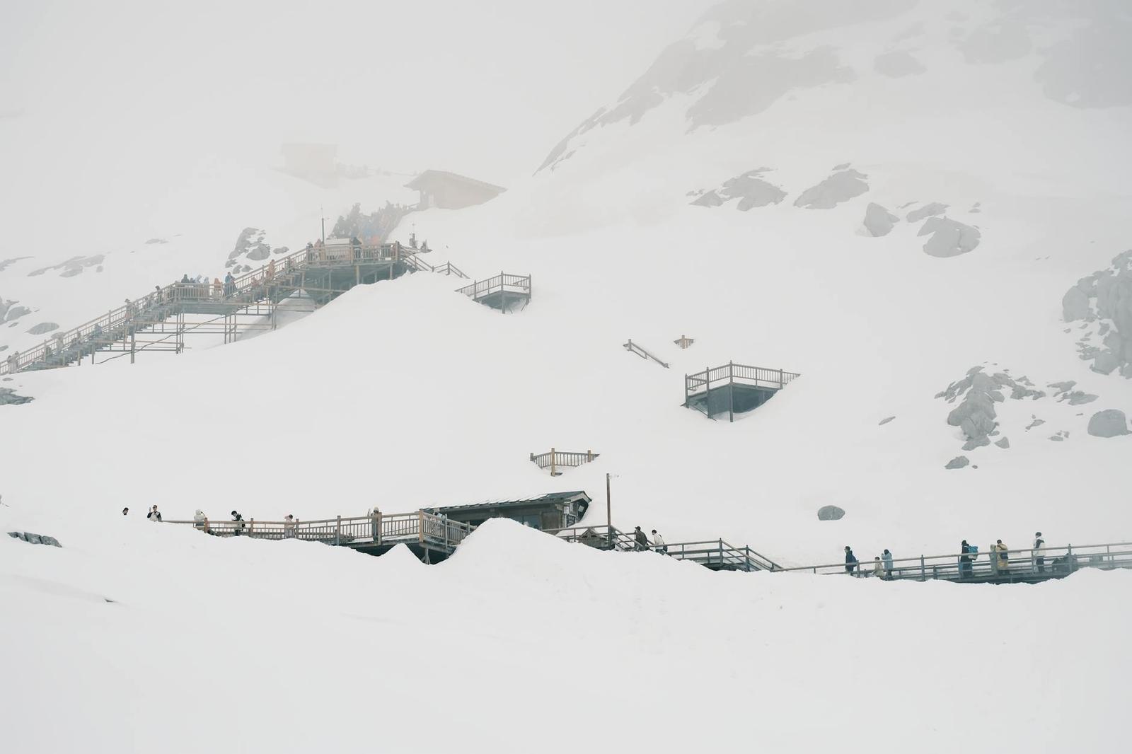 Breathtaking view of snow-covered mountains with walkways and tourists, enhancing winter adventure vibes