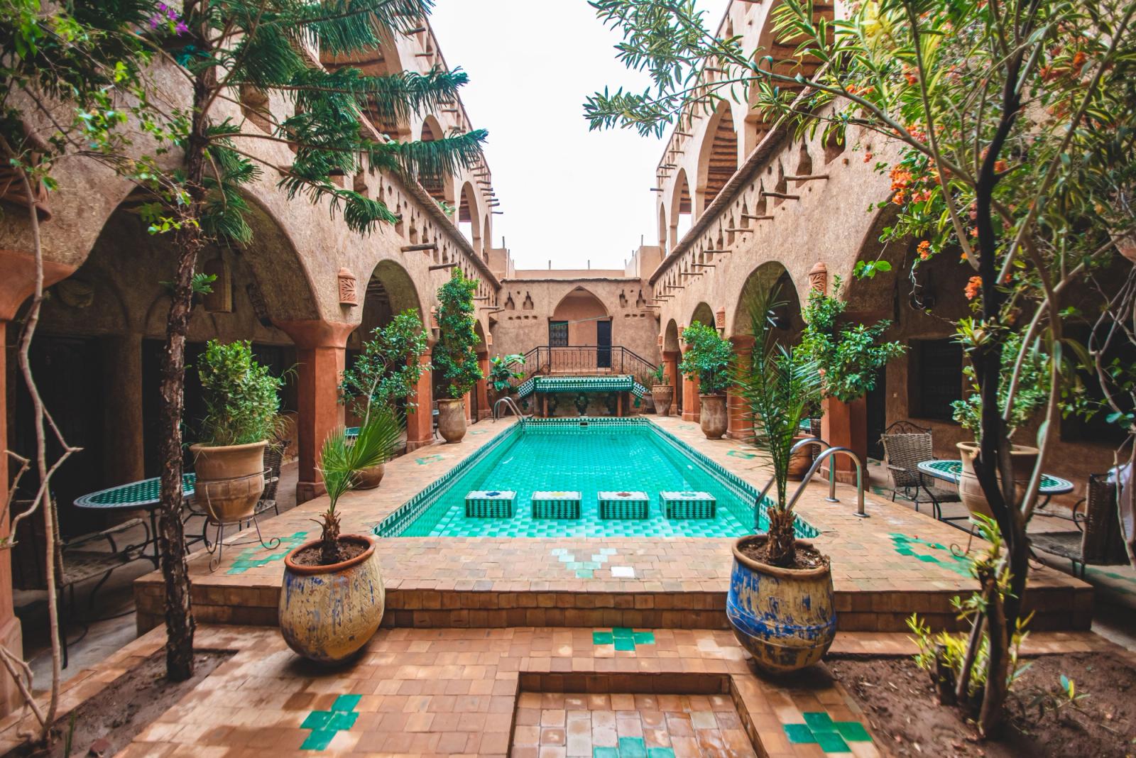 Charming pool courtyard of a traditional riad in Ouarzazate, Morocco, with lush plants and intricate architecture