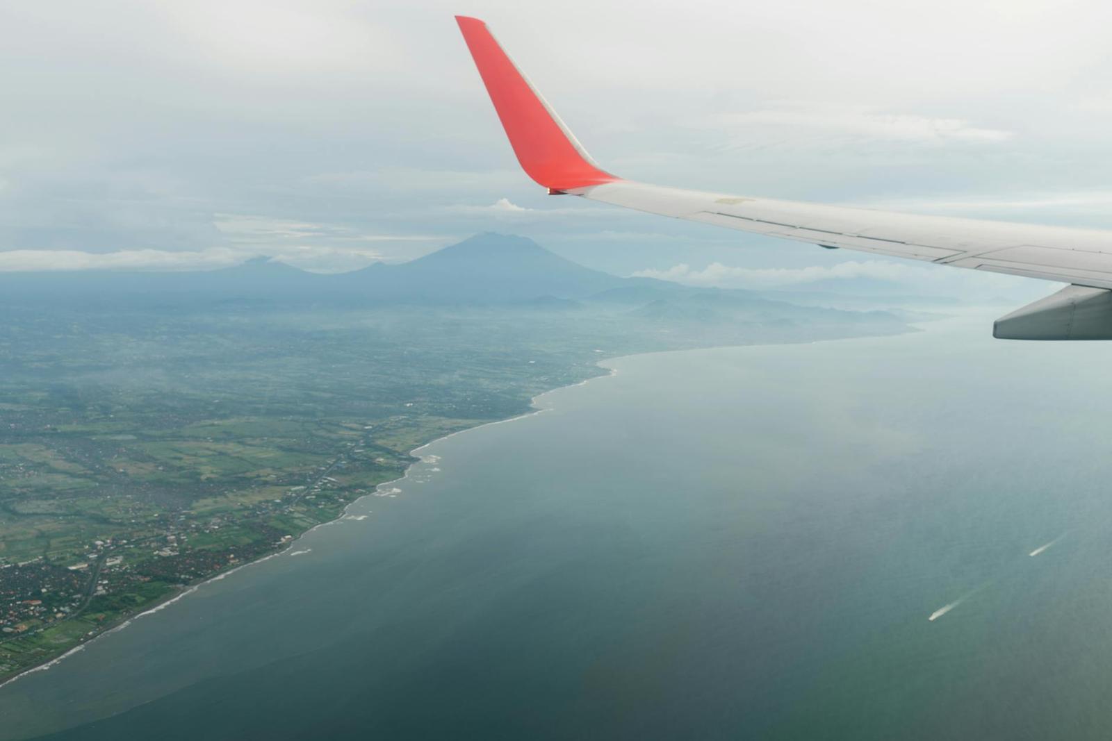 A view from an airplane window of coastline and a distant volcano