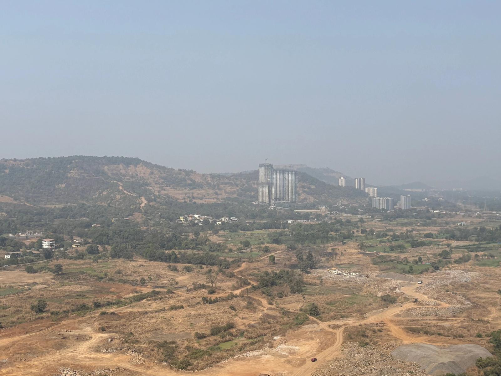A scenic view of Pune's countryside with hills and high-rise buildings under a clear sky