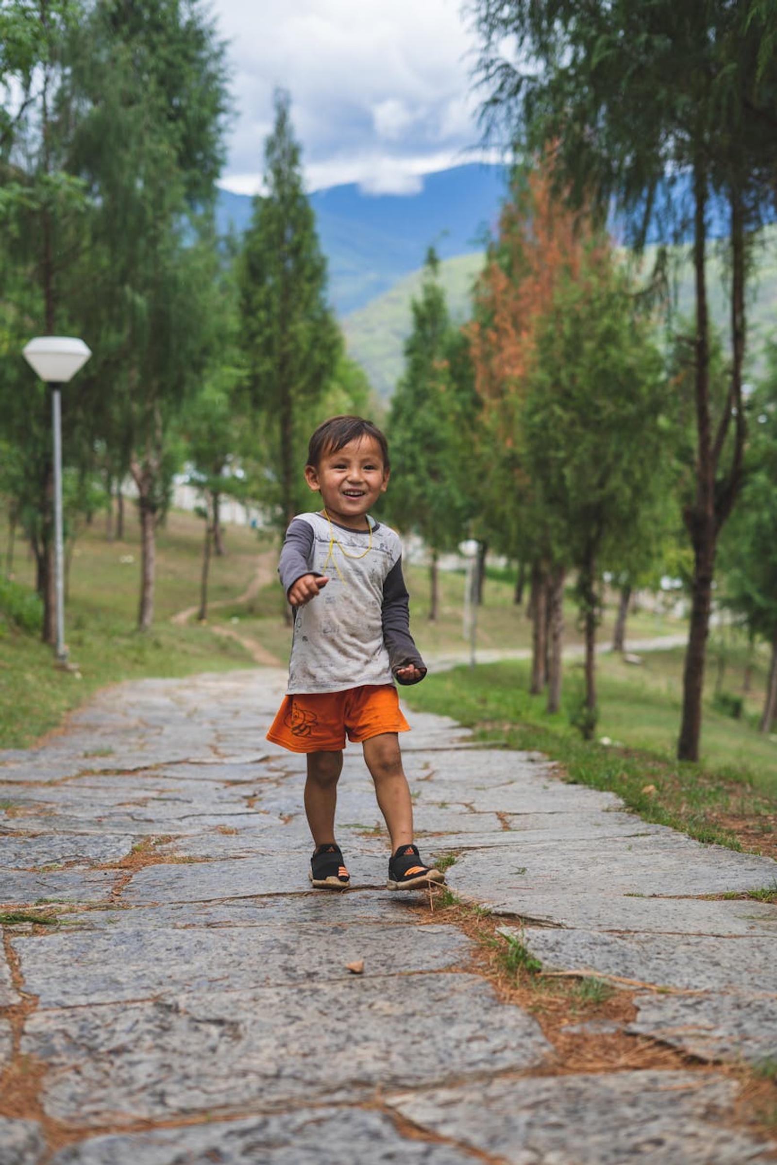A happy South Asian boy walking in a scenic park in Paro, Bhutan, surrounded by lush greenery