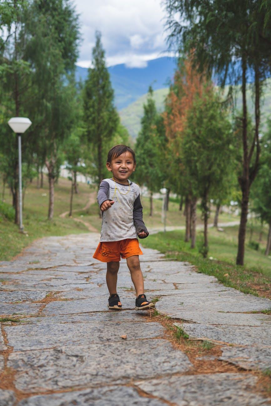 A happy South Asian boy walking in a scenic park in Paro, Bhutan, surrounded by lush greenery