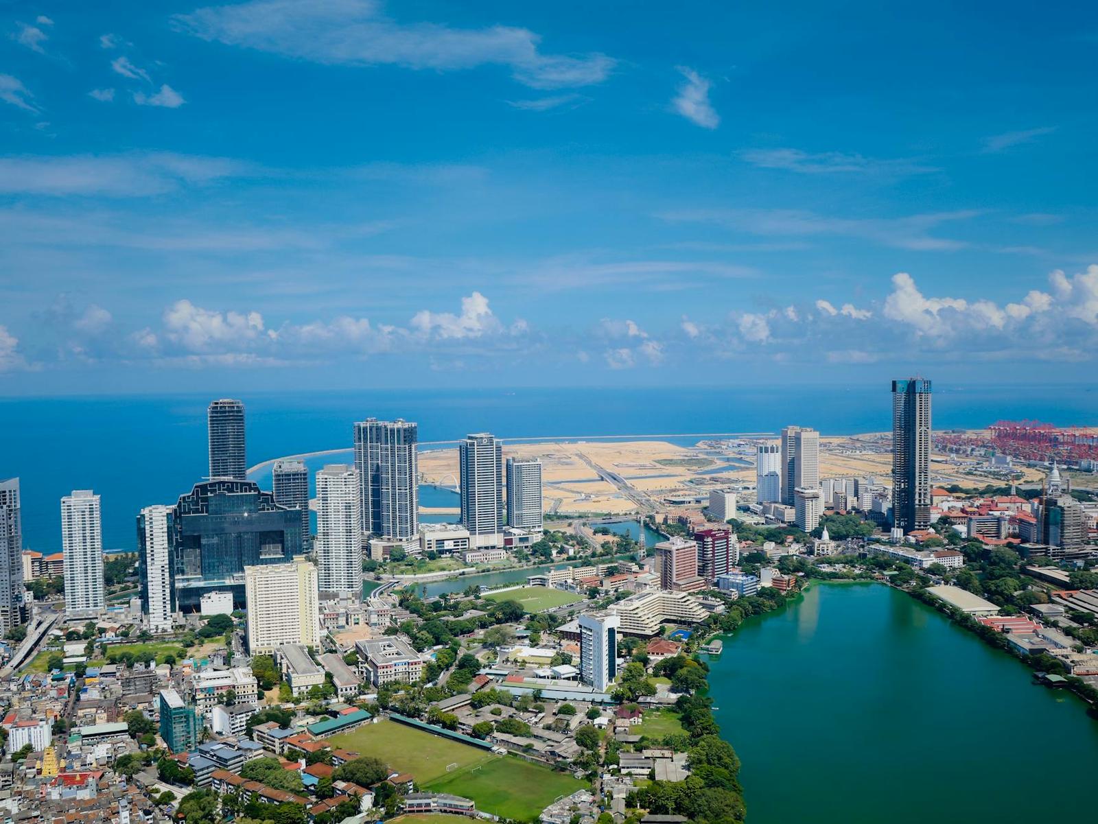 Aerial view of a coastal city skyline with skyscrapers beside a green lagoon