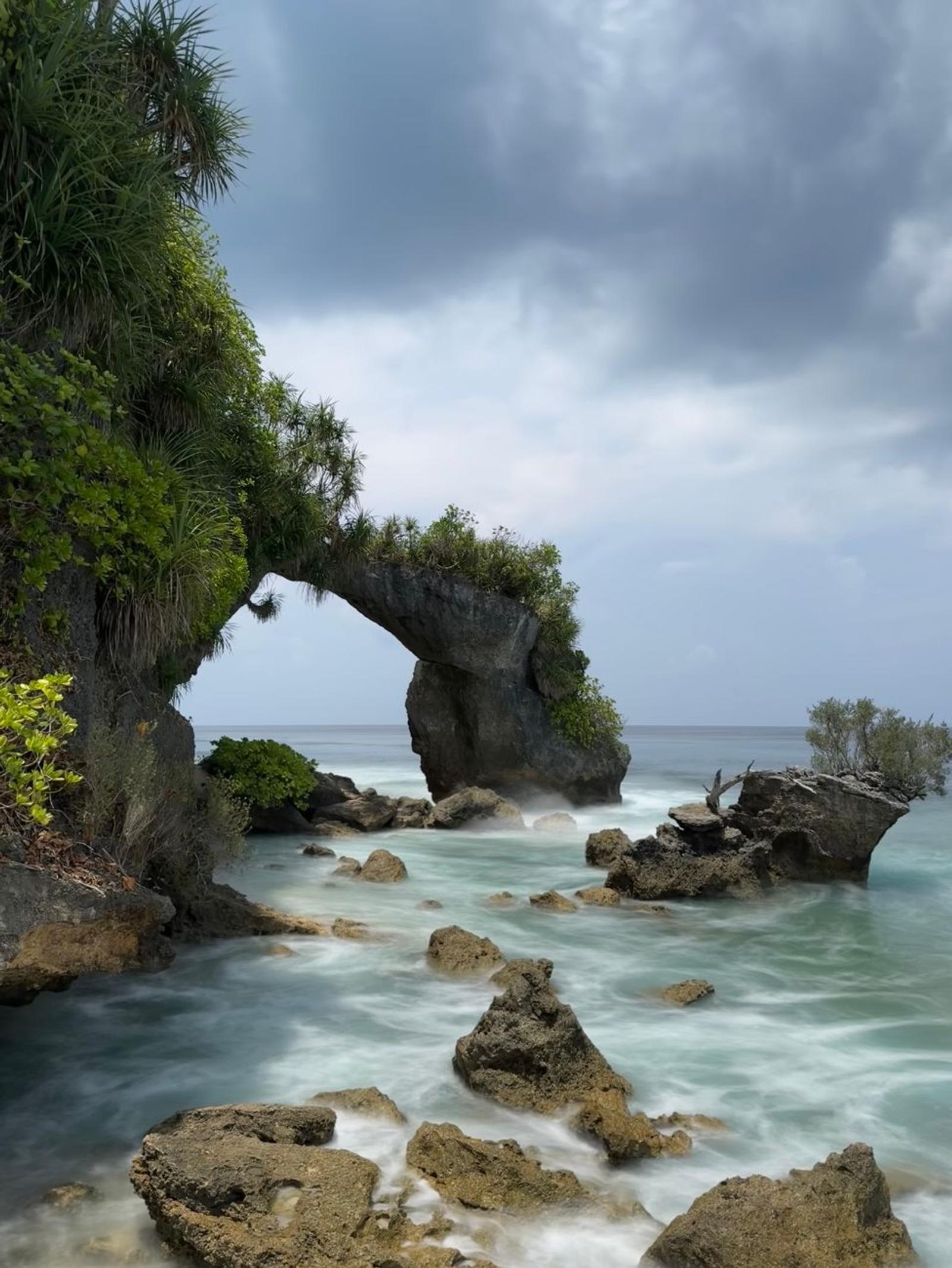 Stunning view of natural rocky arch at Lakshmanpur Beach, India, with lush greenery and ocean waves