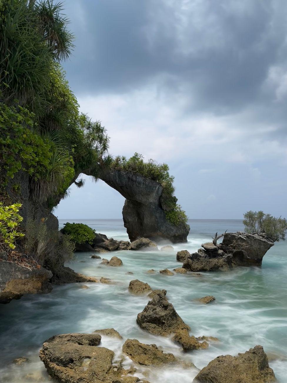 Stunning view of natural rocky arch at Lakshmanpur Beach, India, with lush greenery and ocean waves