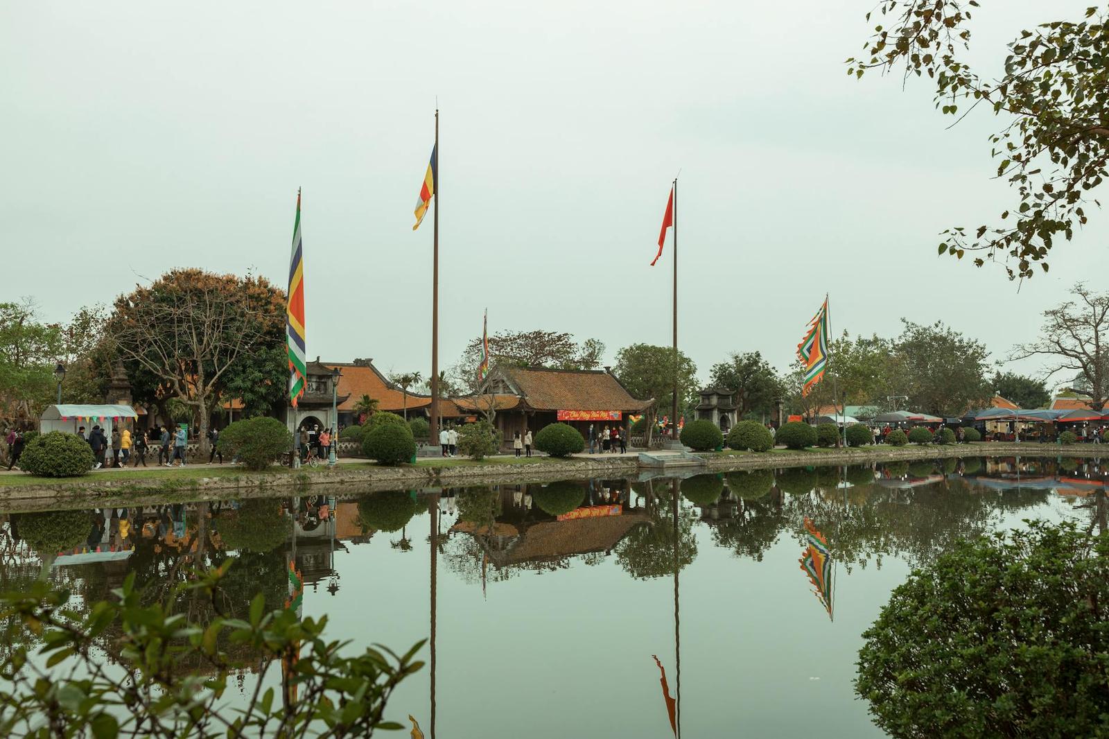 Temple pavilion with colourful flags reflected in a still lakeside pond