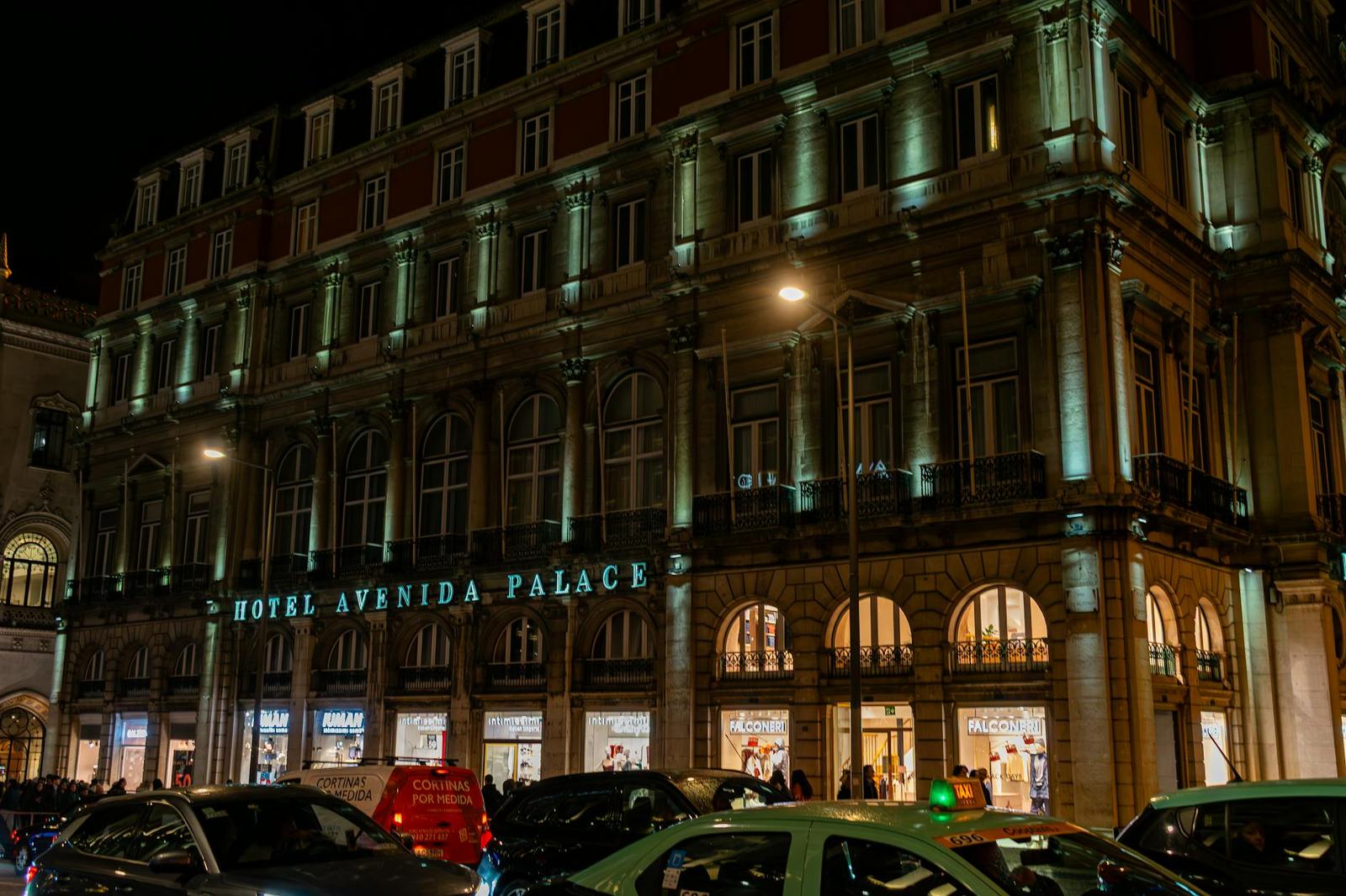 Illuminated hotel building at night with taxis and shopfronts along the street