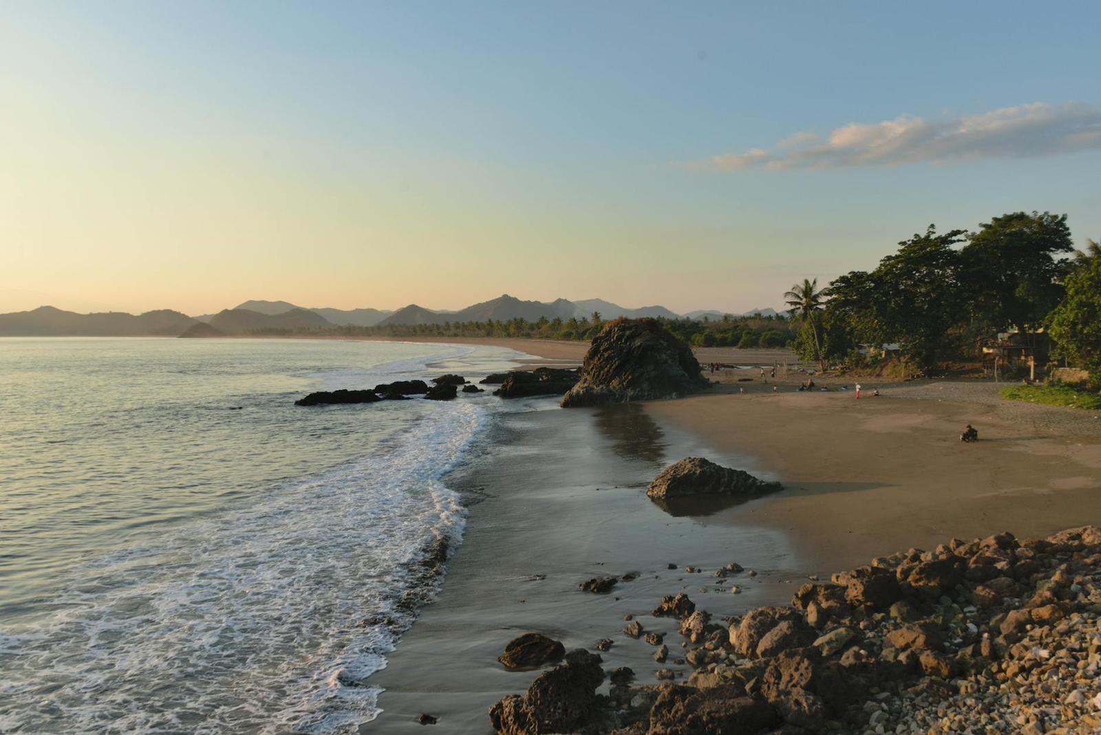 A quiet sandy beach with a rocky outcrop at dawn