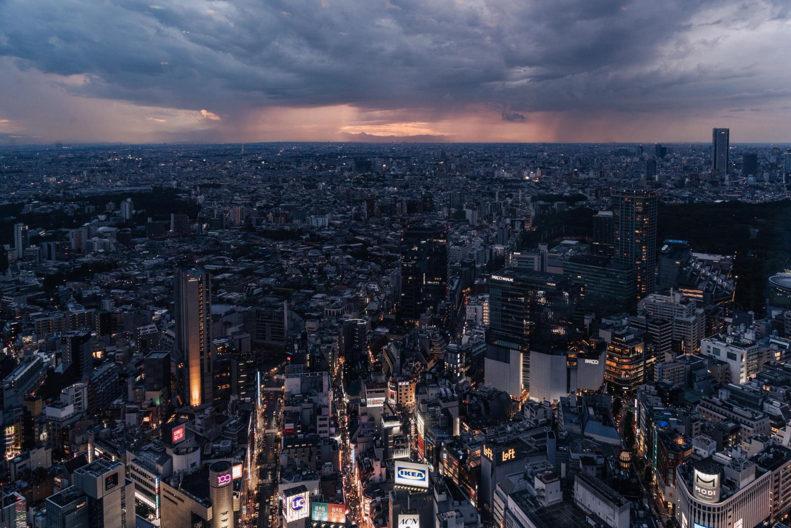 Aerial view of Tokyo cityscape during twilight with storm clouds gathering, showcasing urban lights