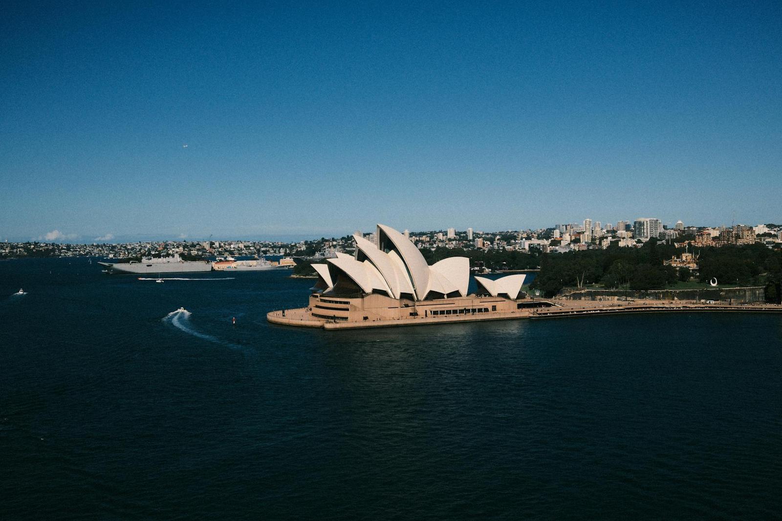 An opera house with white sail roofs seen from the air above a harbour