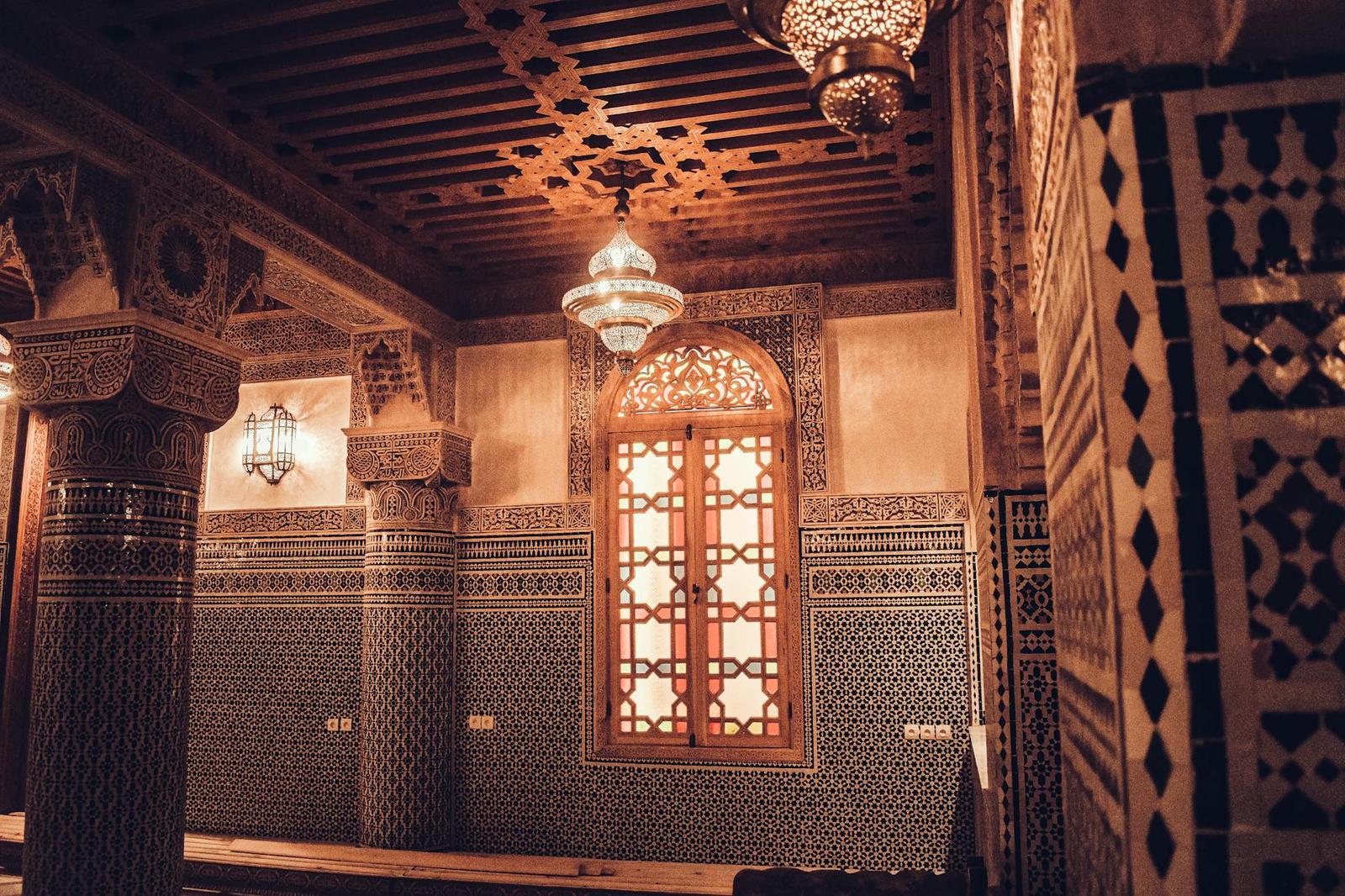 An ornately tiled riad interior with carved wooden ceiling and hanging lantern