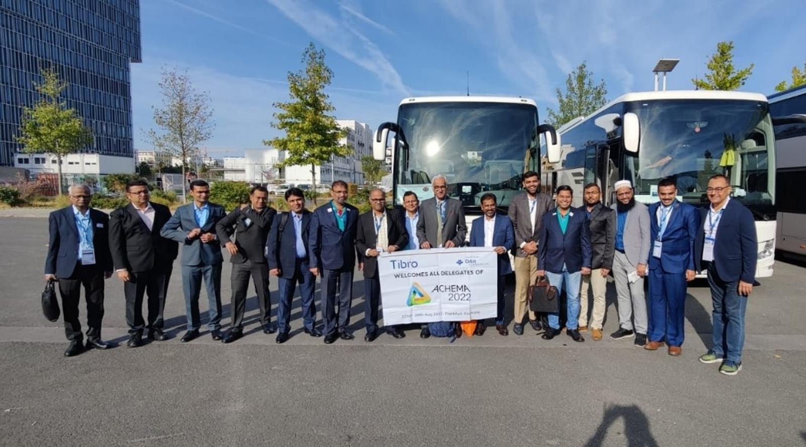 Group of people in formal attire posing in front of two large buses
