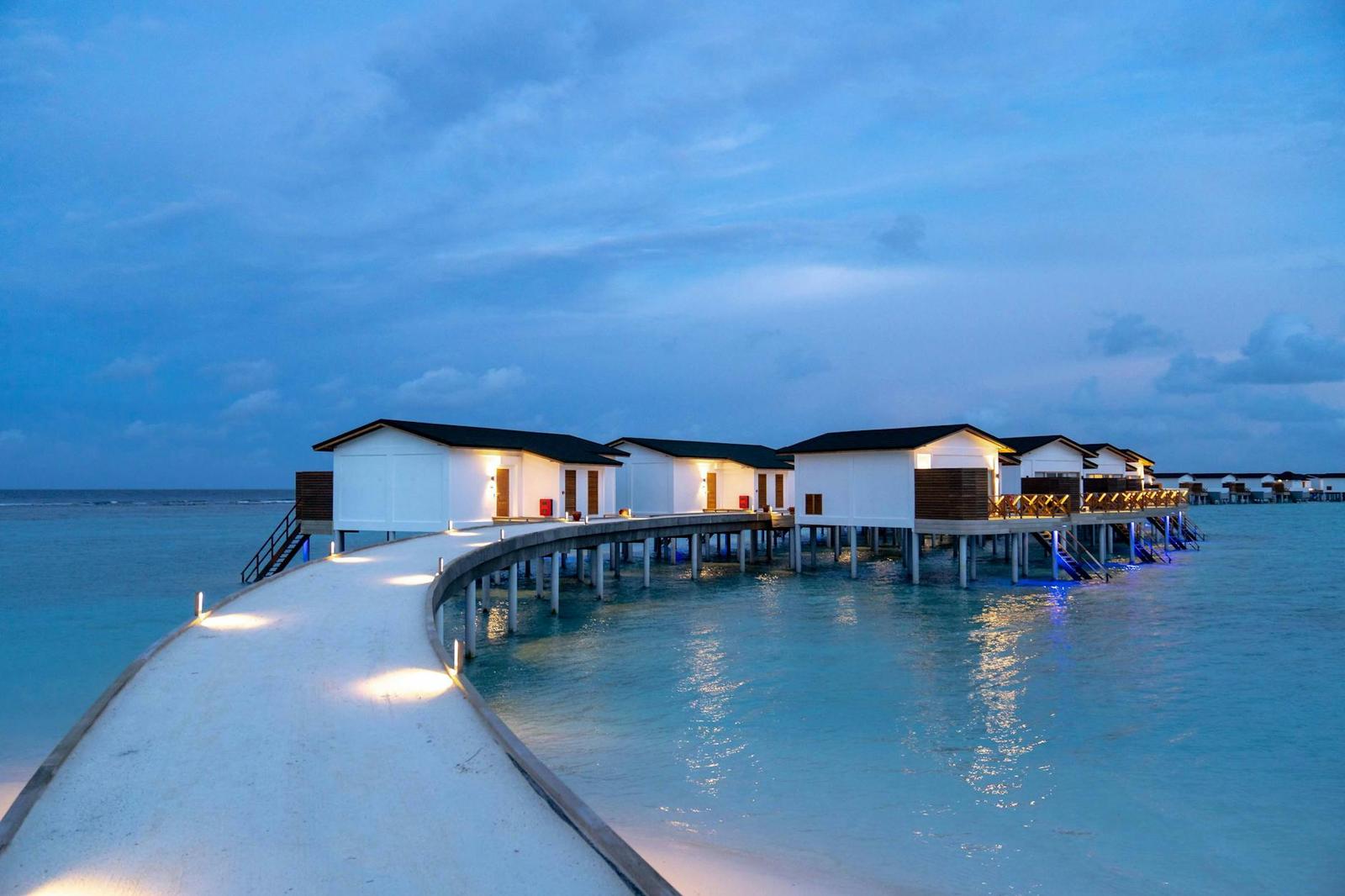 Overwater bungalows on stilts lit up at dusk