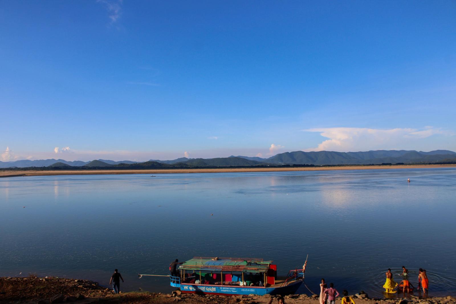 A calming river scene in India with distant mountains and a colorful boat