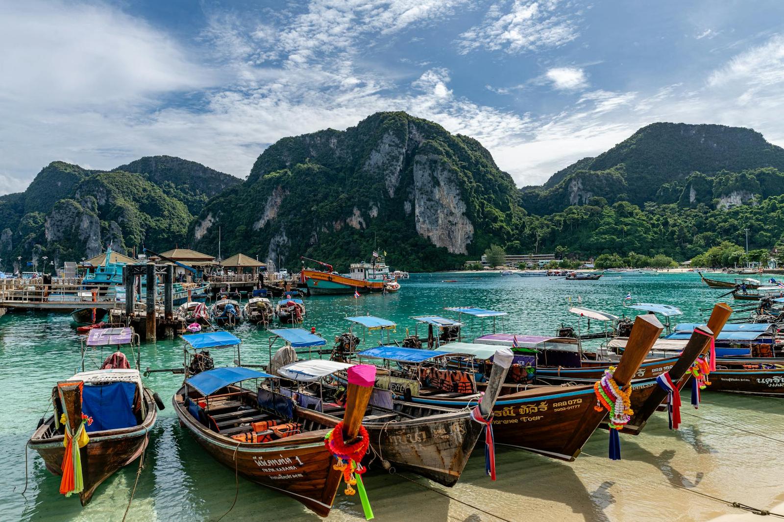 Colorful longtail boats moored on a beach beneath jungle-covered limestone peaks