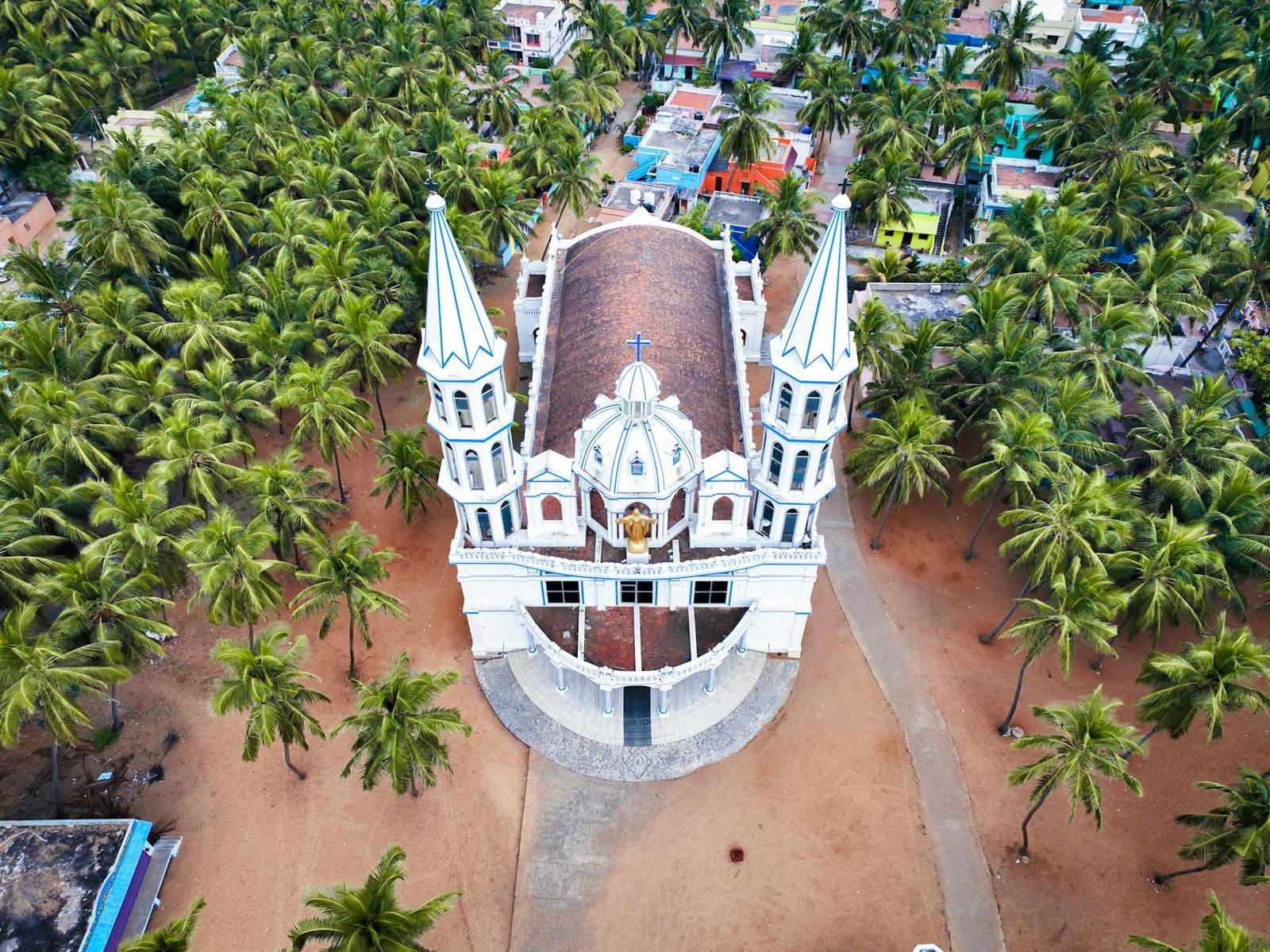 Aerial view of a white twin-spired church surrounded by coconut palms