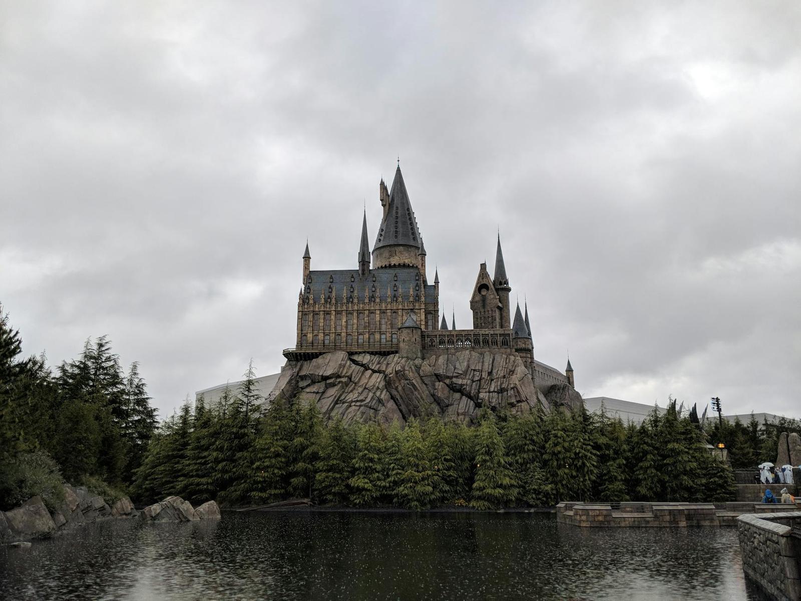 A turreted stone castle reflected in a still lake under an overcast sky