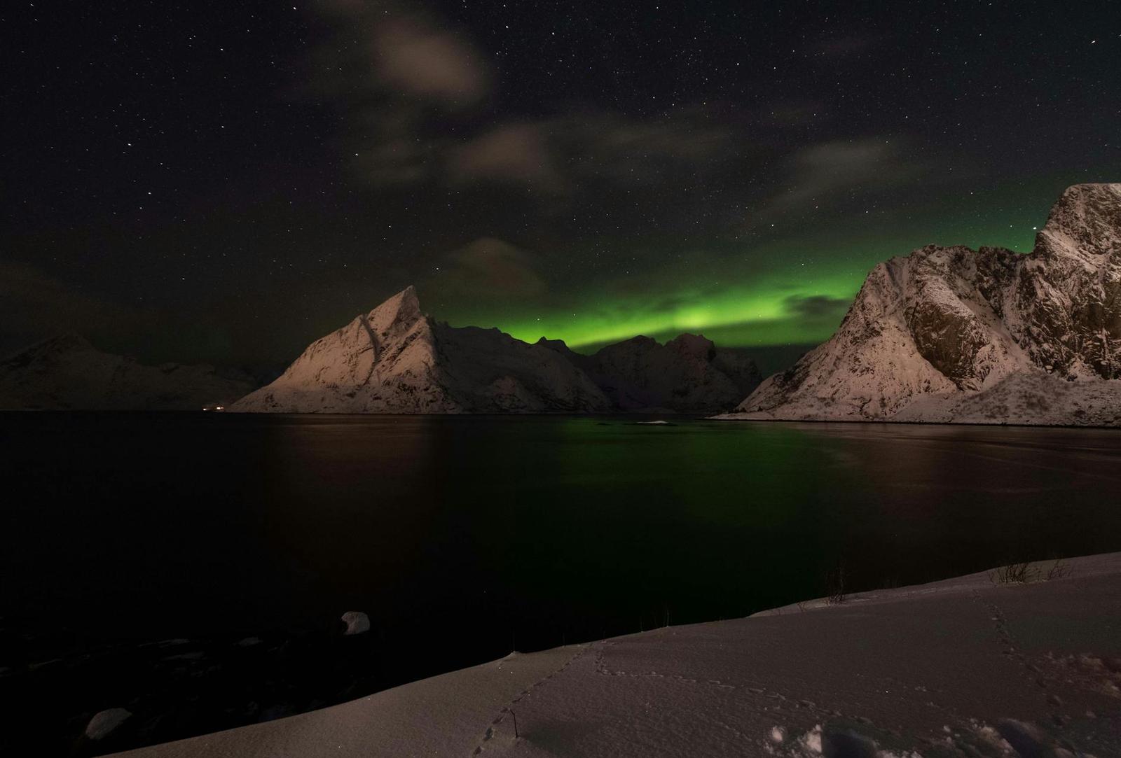 Green aurora lights streaking above snow-capped peaks and a calm dark fjord