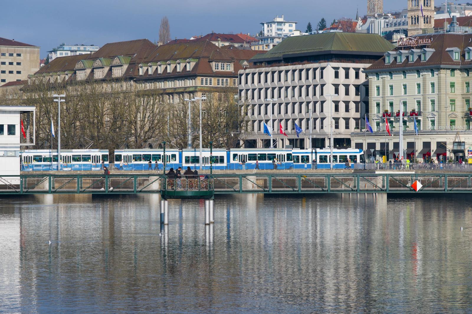 Tram crossing a bridge in Zurich with historic buildings in the background on a clear day