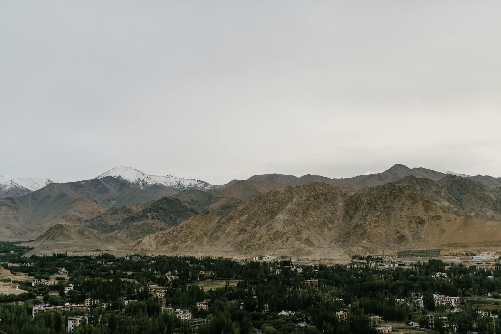 A town nestled among trees below arid mountains and snow-capped peaks