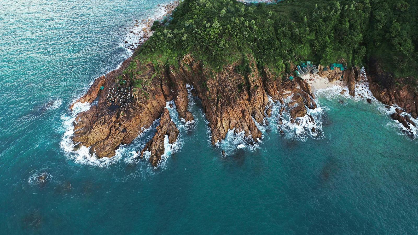 Aerial view of a rocky forested headland meeting turquoise water