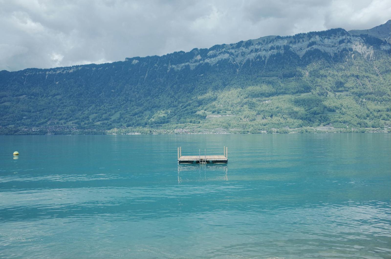 A small floating dock on a turquoise lake beneath cloud-covered mountains