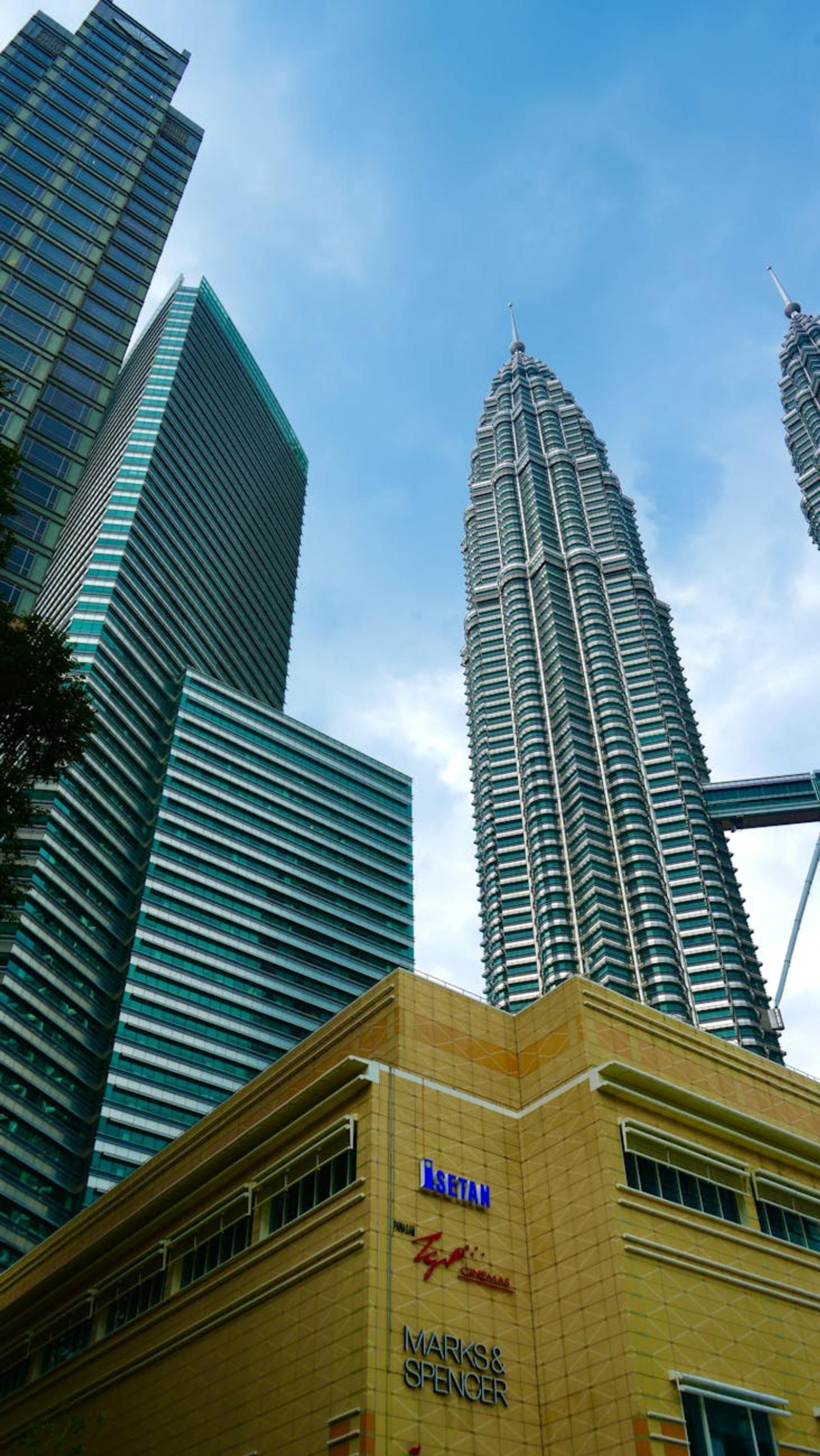 Twin glass skyscrapers with ornate spires rising above a shopping mall entrance