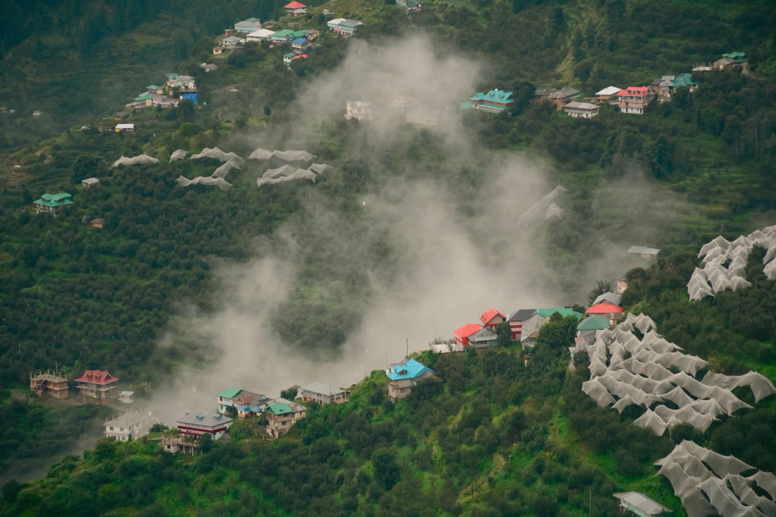 Scenic aerial view of a mist-covered village nestled in Himachal Pradesh, India, surrounded by lush greenery