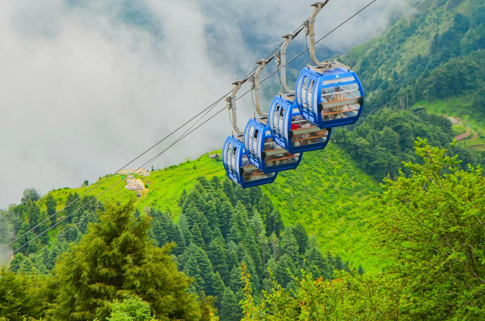 Blue cable car gondolas suspended over misty forested hillsides