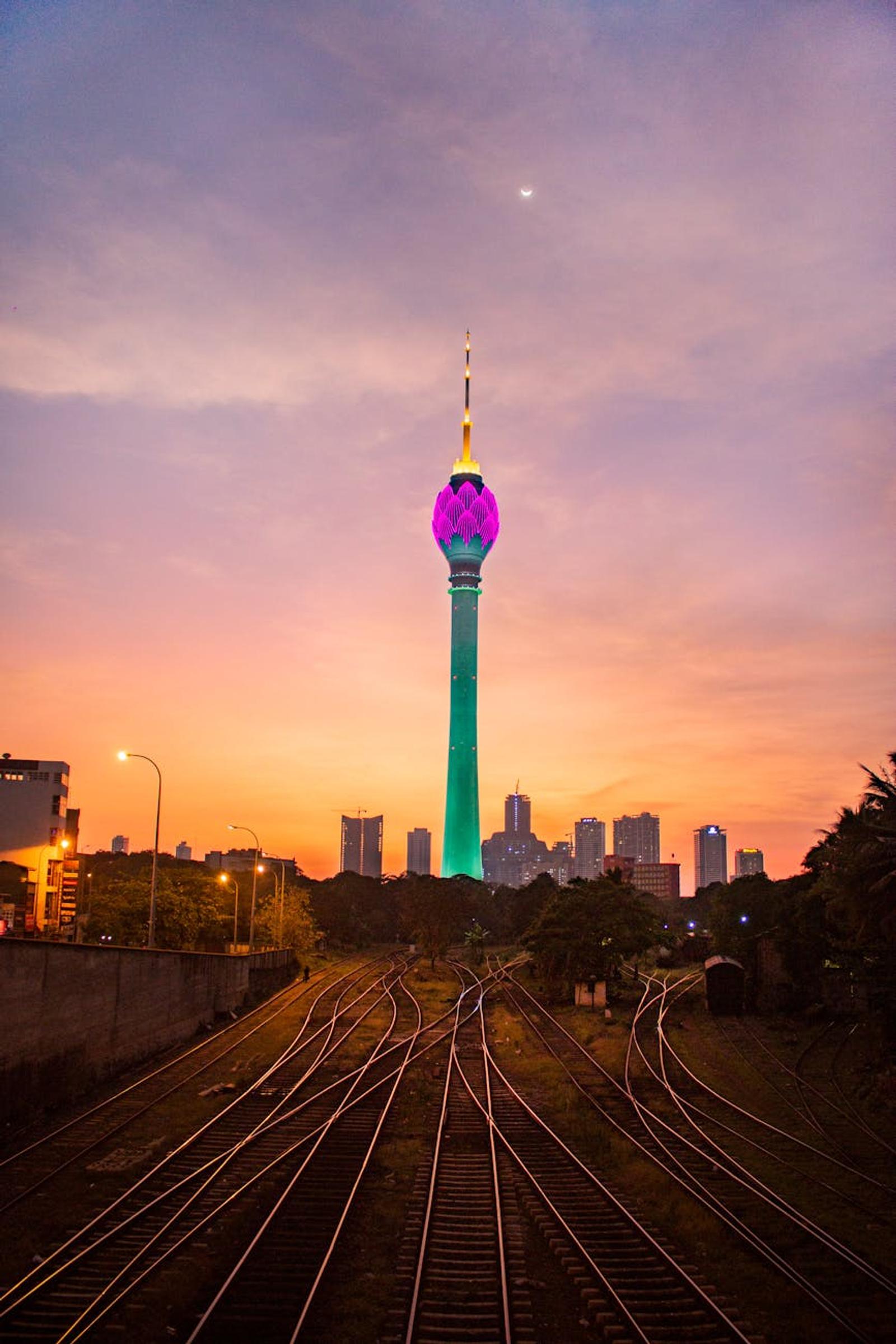 View of illuminated Colombo Lotus Tower at sunset with railway foreground in Sri Lanka