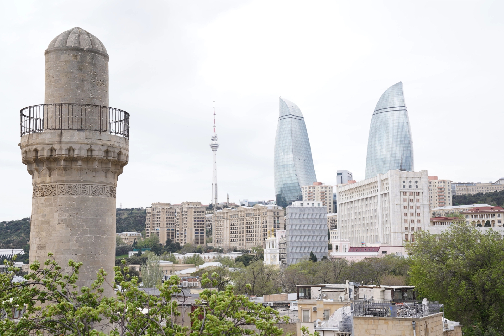 Scenic view of Baku's architectural landmarks including Flame Towers and a historic minaret under a cloudy sky