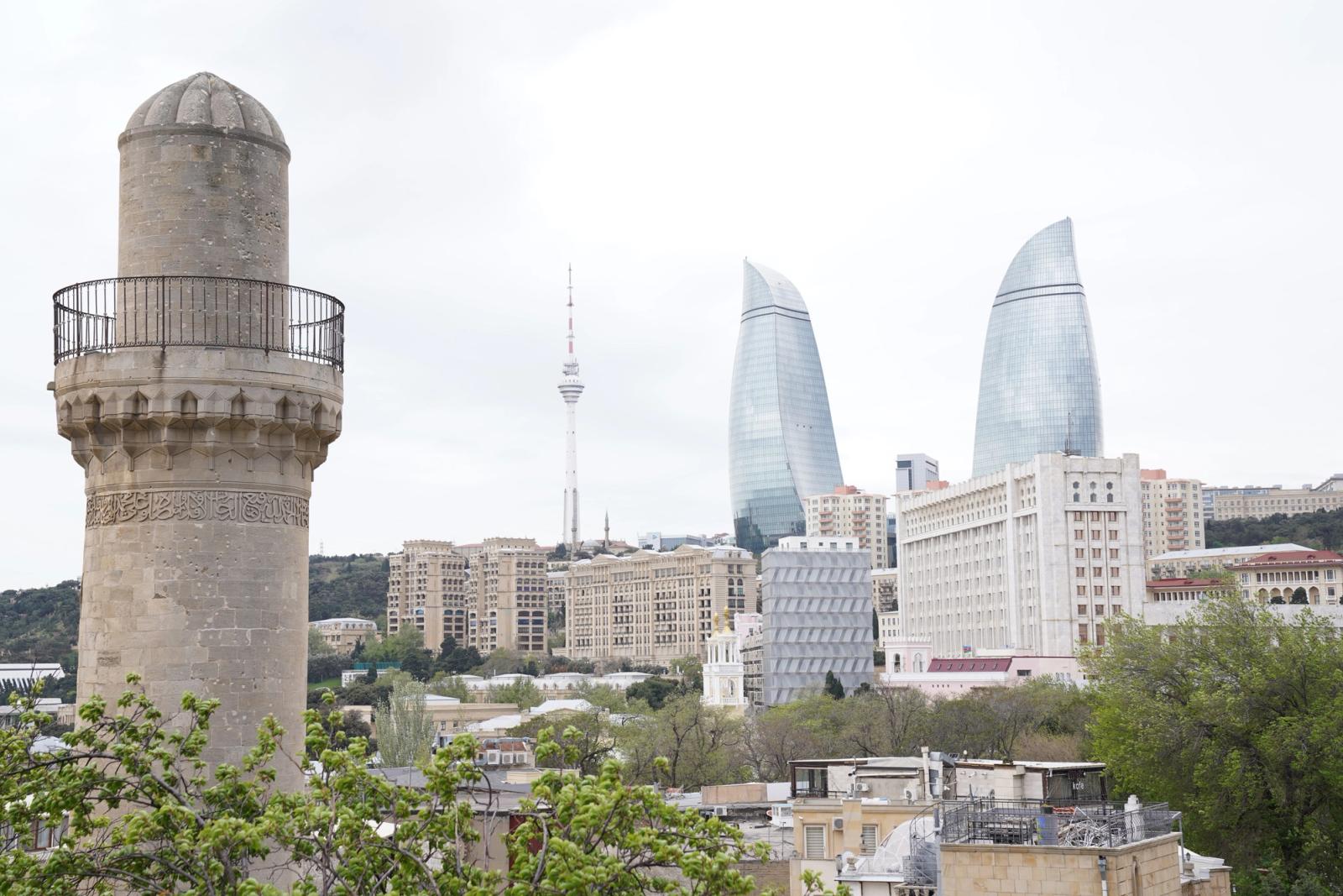 Scenic view of Baku's architectural landmarks including Flame Towers and a historic minaret under a cloudy sky