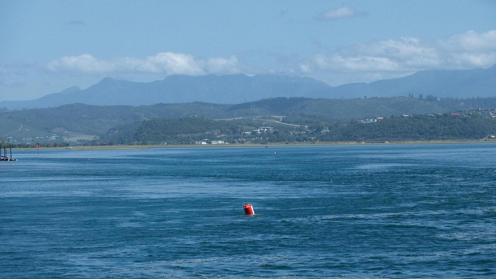 Red buoy floating in a calm bay backed by distant mountains