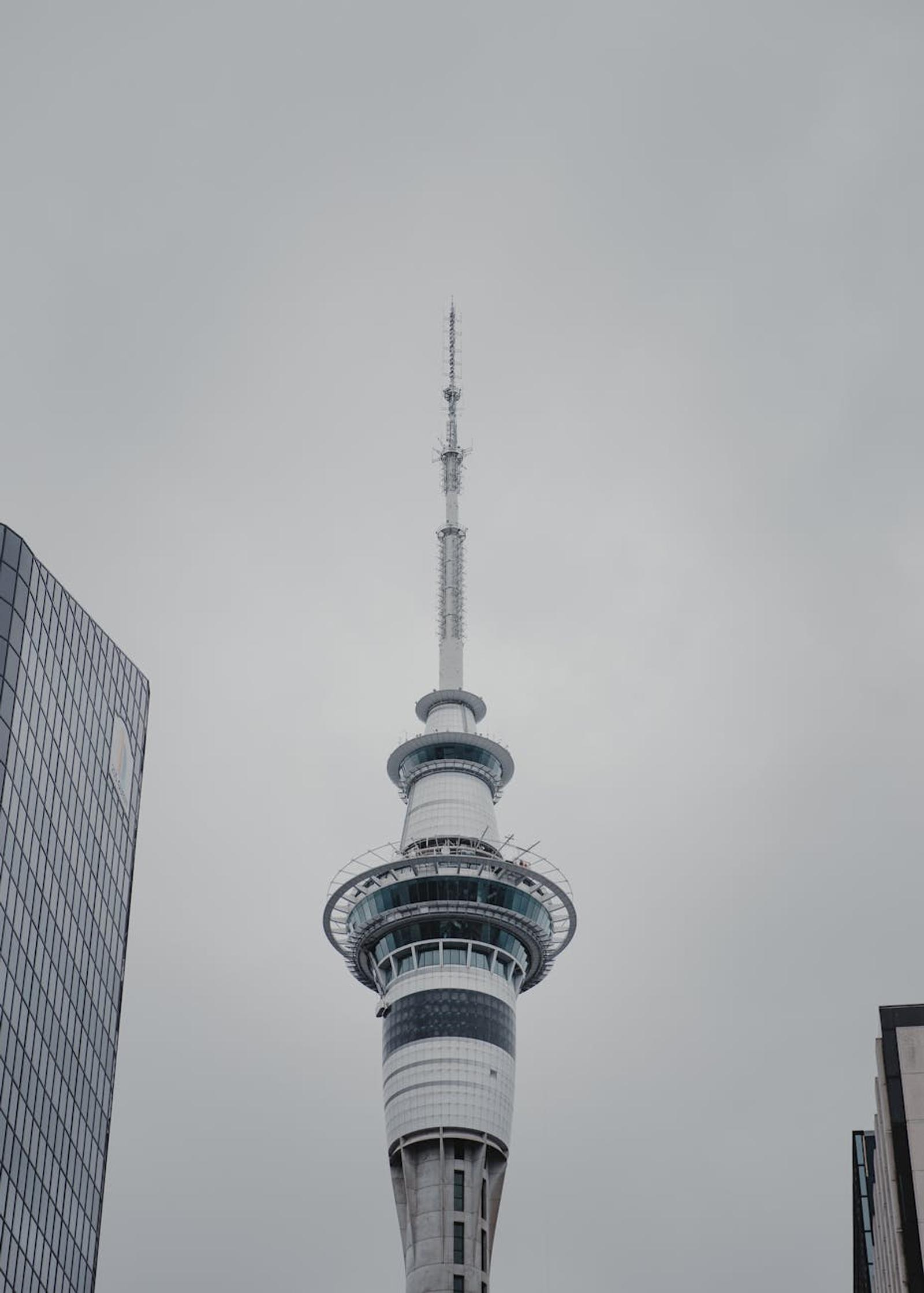 Slender spire of an observation tower against an overcast sky between buildings