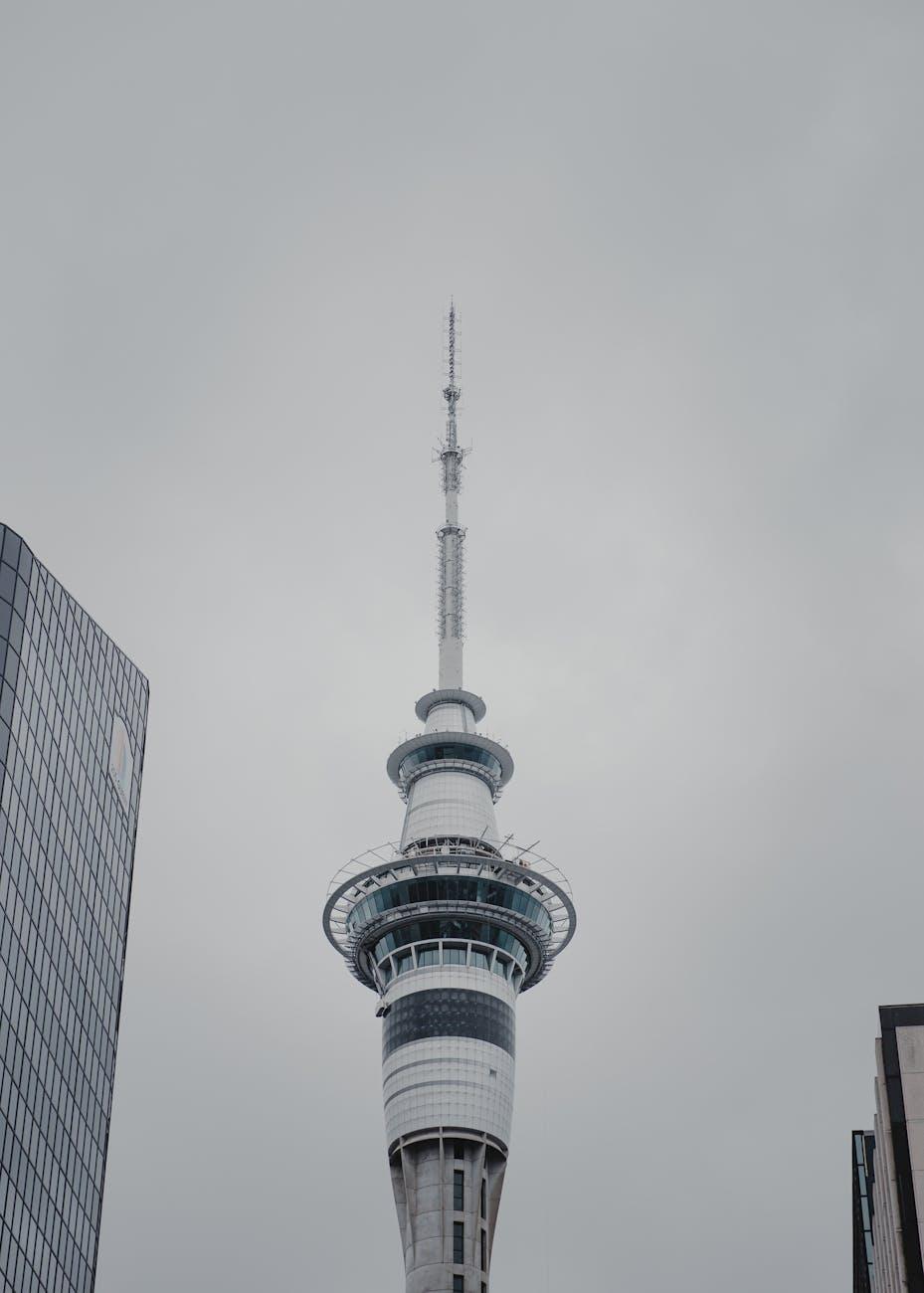 Slender spire of an observation tower against an overcast sky between buildings