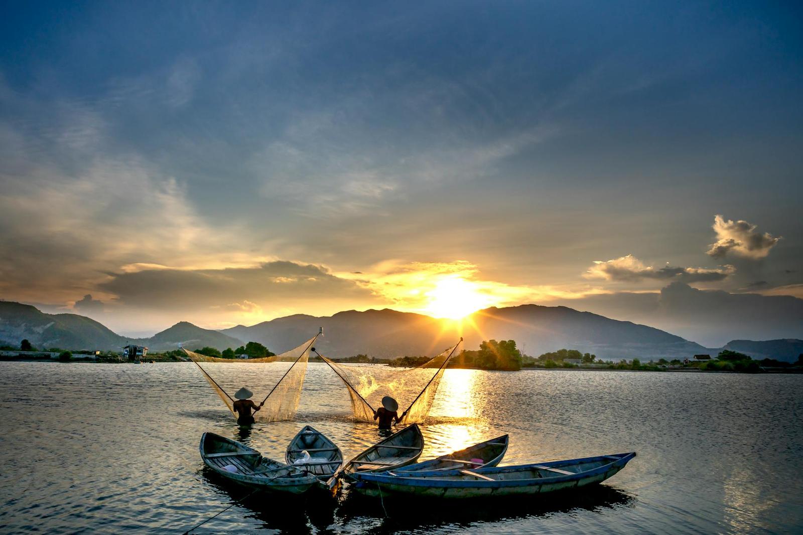 Two fishermen casting nets from canoes on a lake at golden sunset