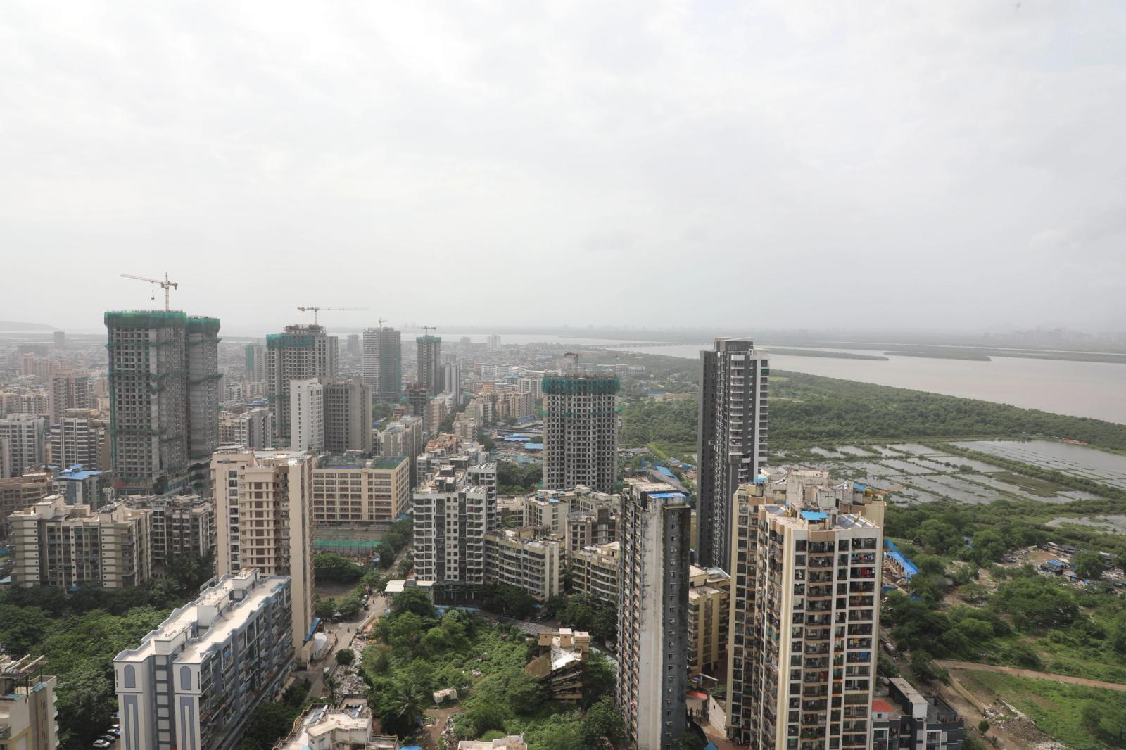 High-angle view of urban cityscape featuring skyscrapers, greenery, and a river under a cloudy sky