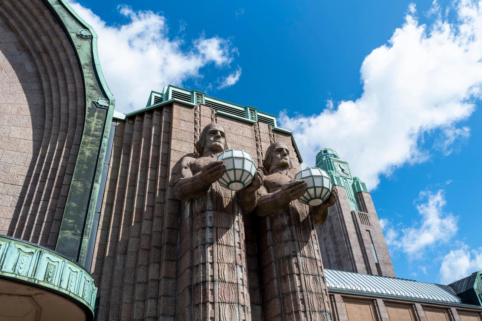 Art Deco facade of Helsinki Central Station with iconic stone lantern figures against a blue sky