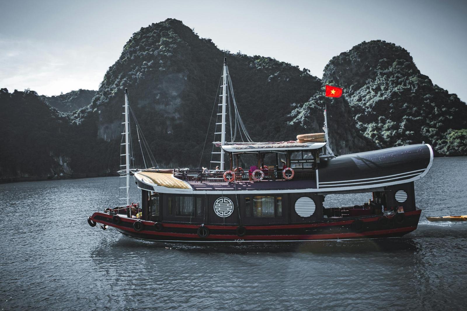 A traditional wooden junk boat with a small flag sailing past limestone cliffs
