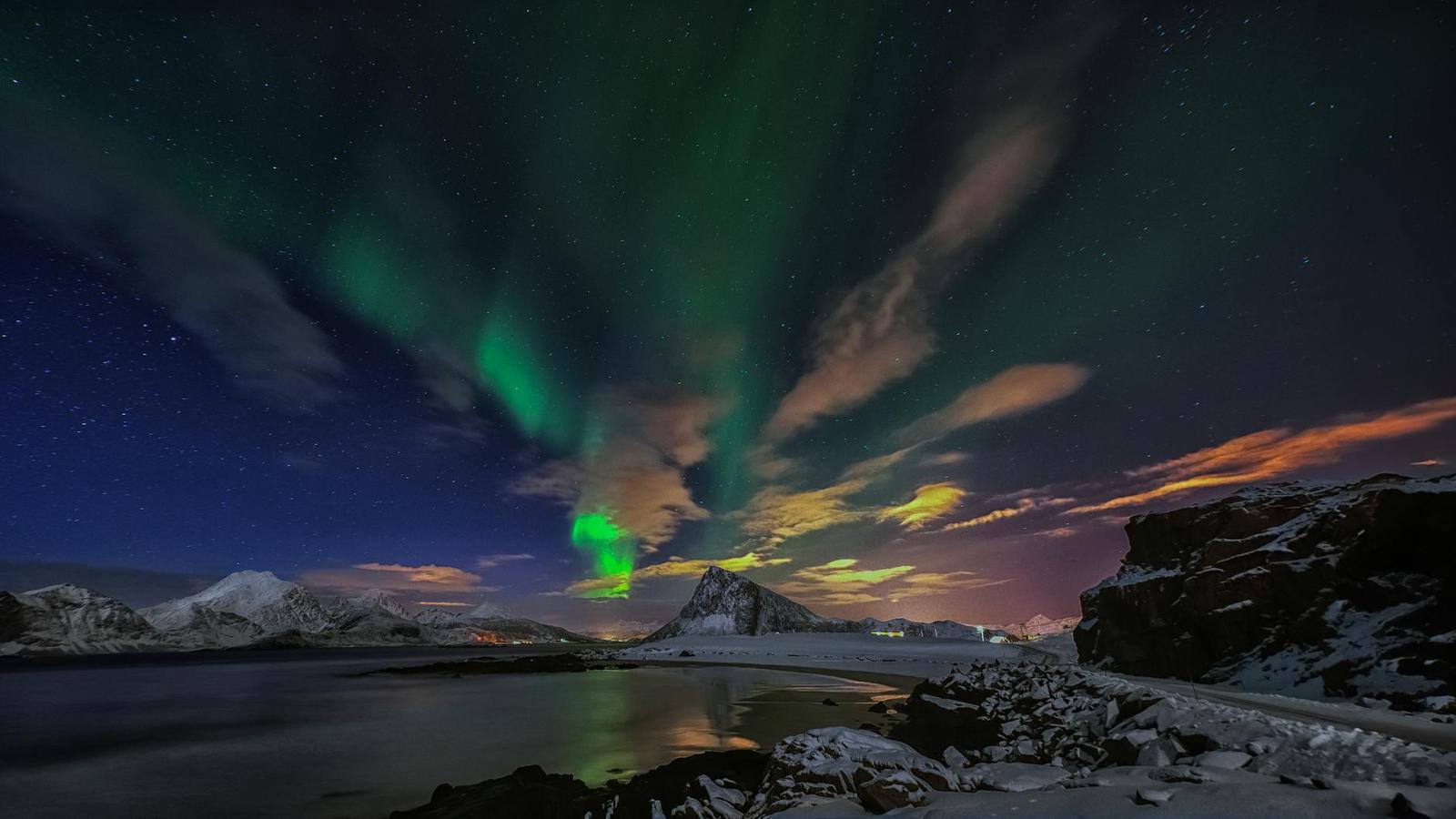 Green aurora ribbons over a snowy shoreline at dusk