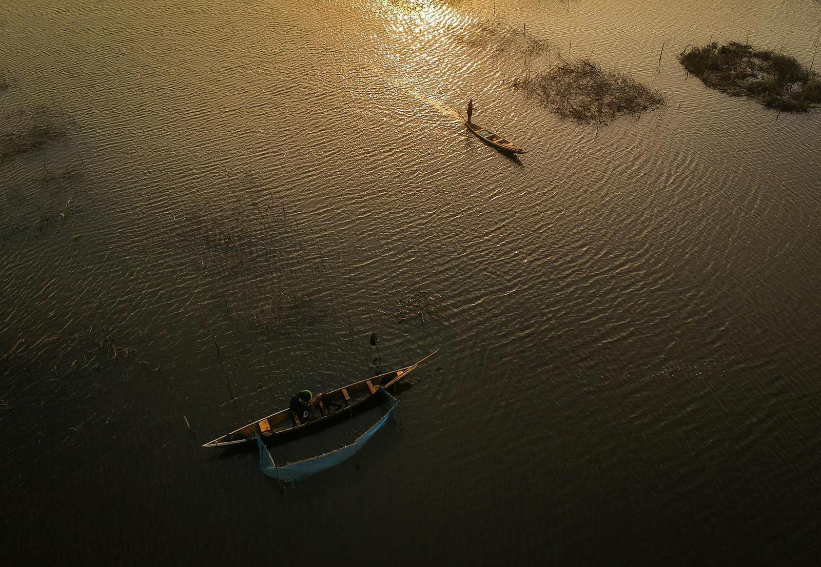 A fisherman paddling a wooden canoe across still water at golden hour