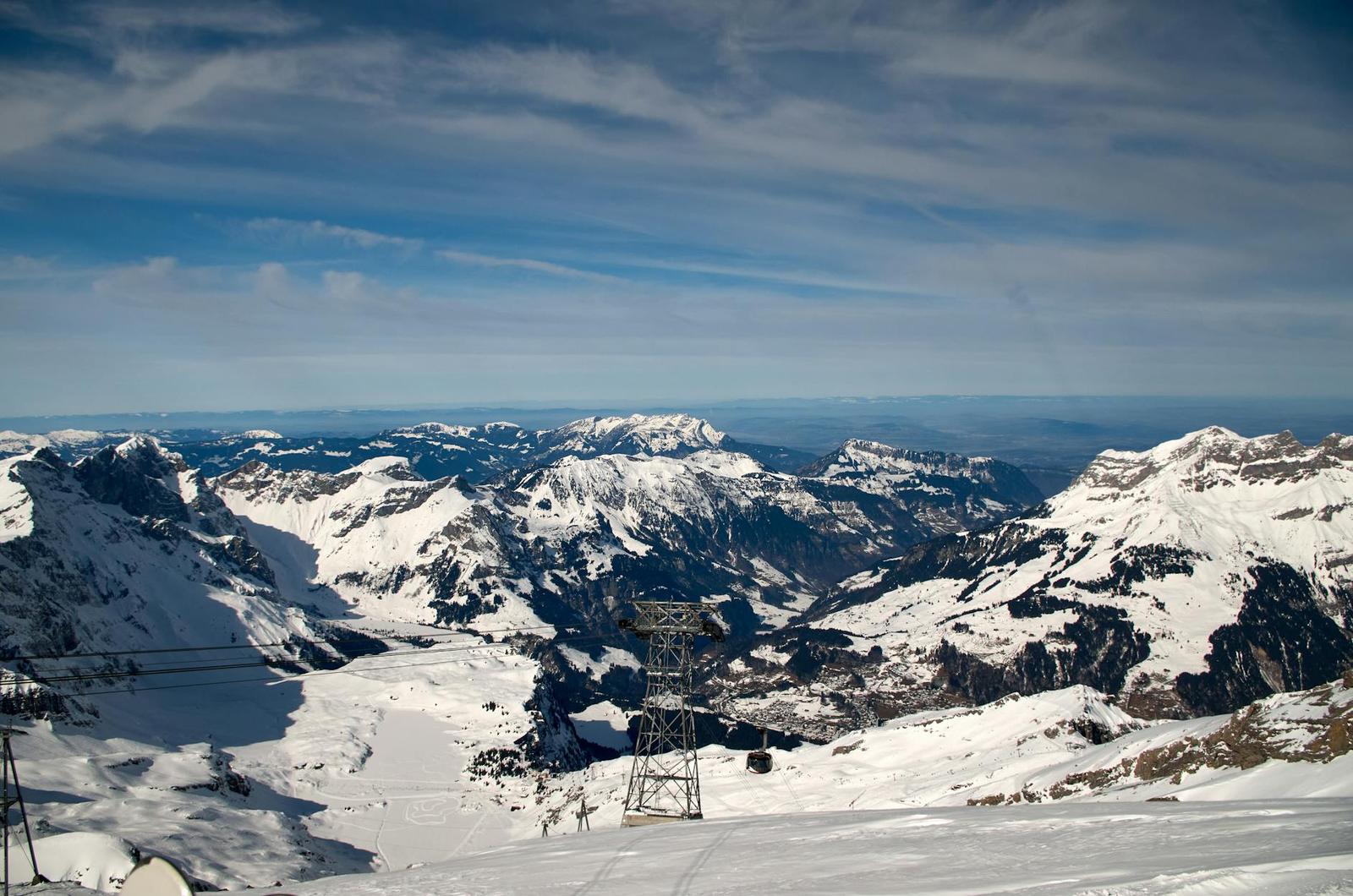 A cable car pylon rising from a snowfield above a deep alpine valley
