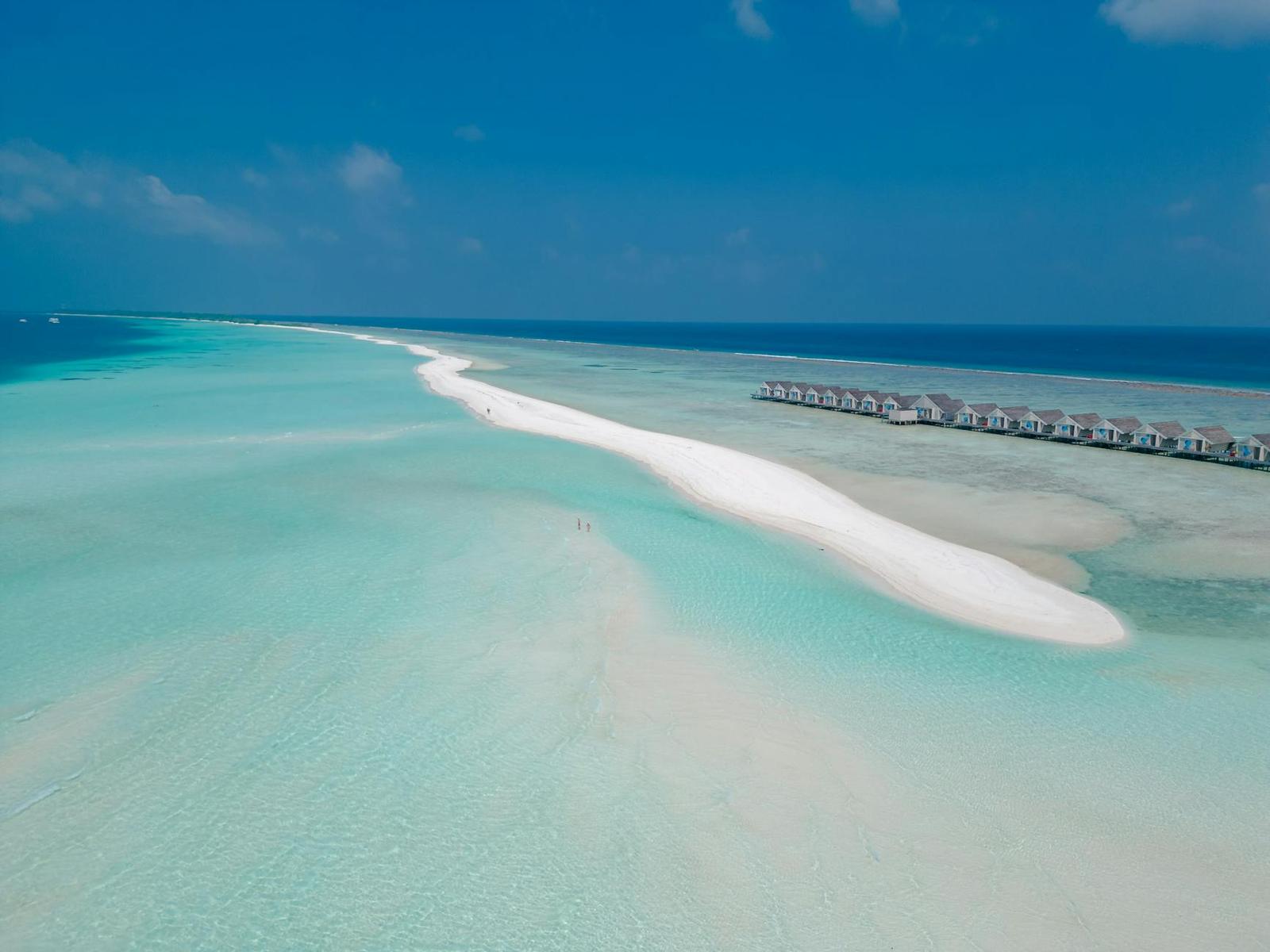 Aerial view of a sandbar stretching toward a row of overwater villas
