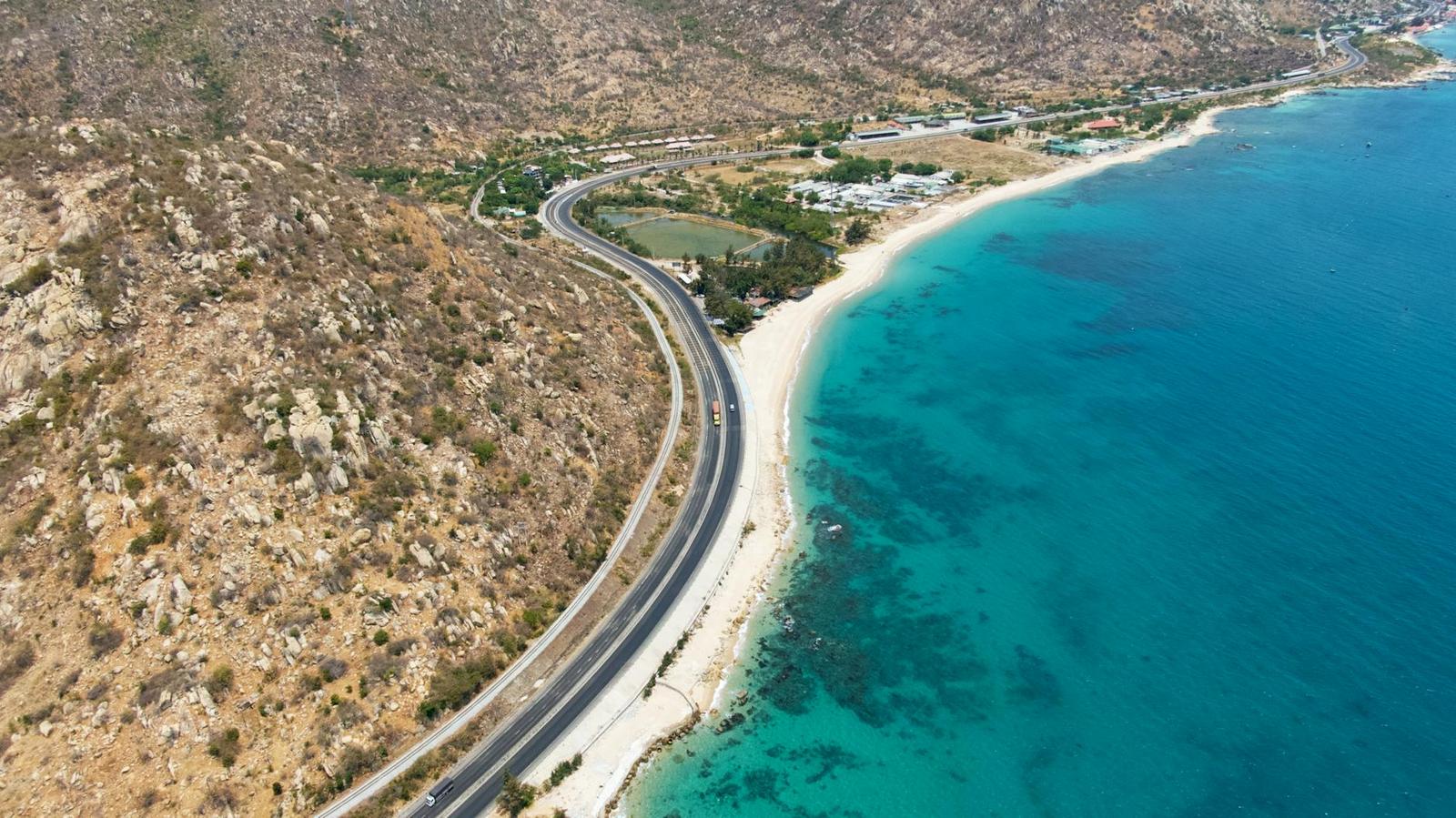 Coastal road winding along a dry hillside beside a turquoise bay