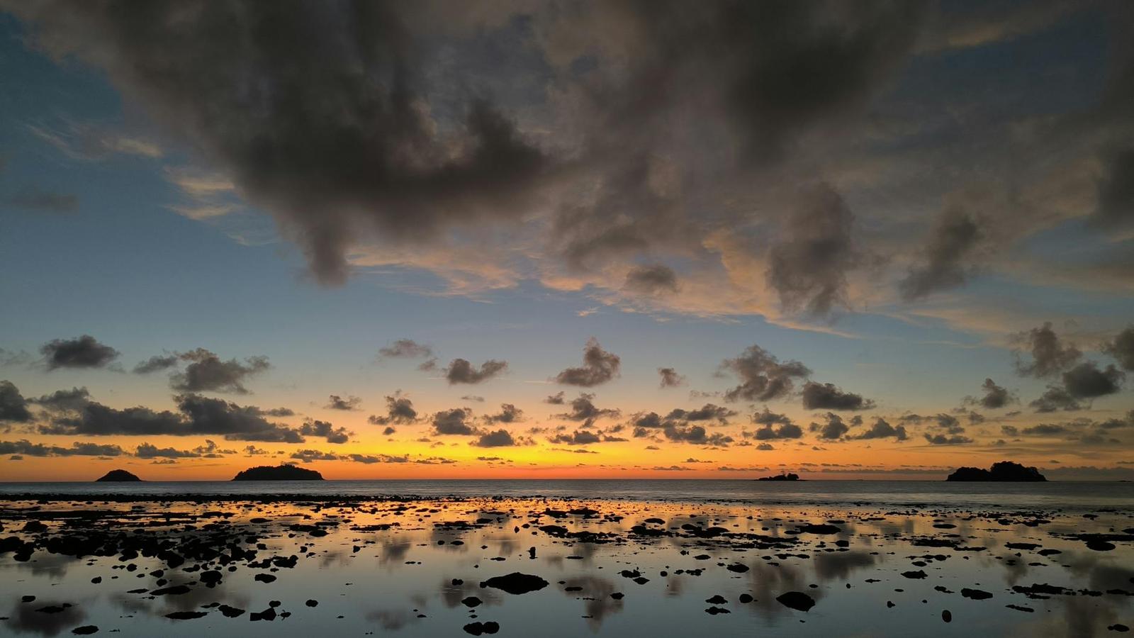 Small islands silhouetted against a glowing sunset sky over calm water