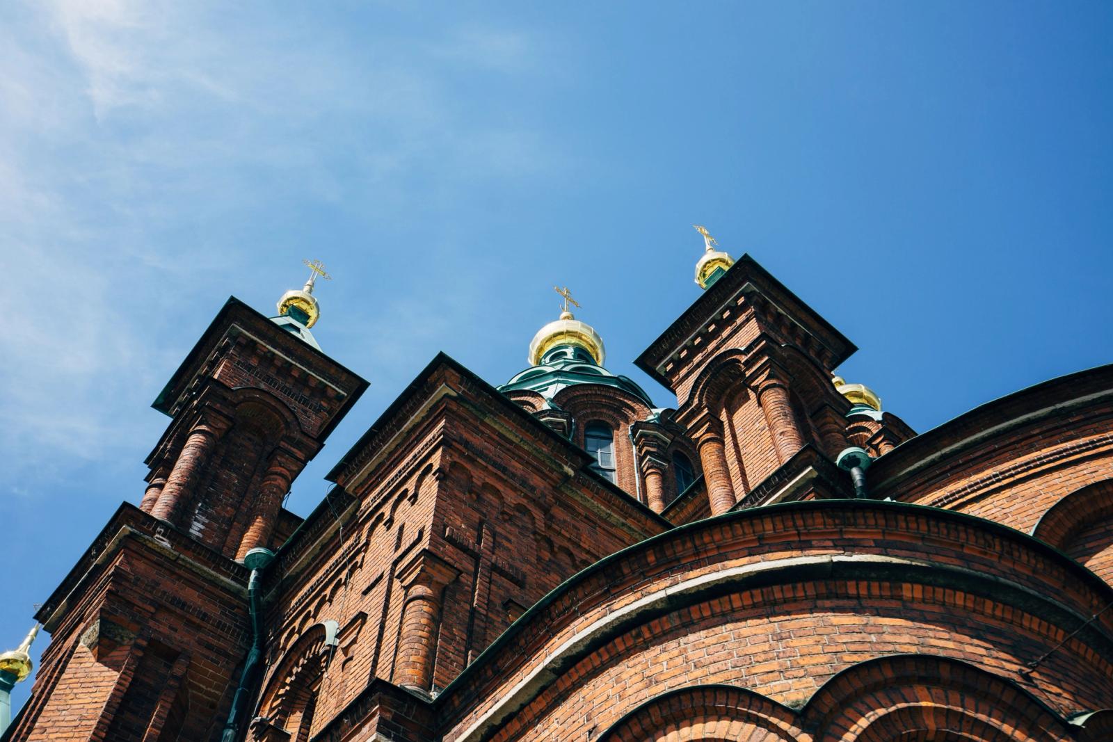 A low-angle view capturing the gold-domed architecture of Helsinki's iconic Orthodox Cathedral under a blue sky