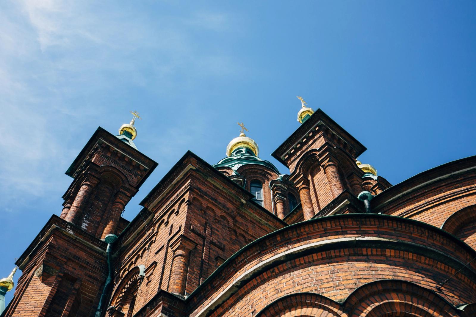 A low-angle view capturing the gold-domed architecture of Helsinki's iconic Orthodox Cathedral under a blue sky